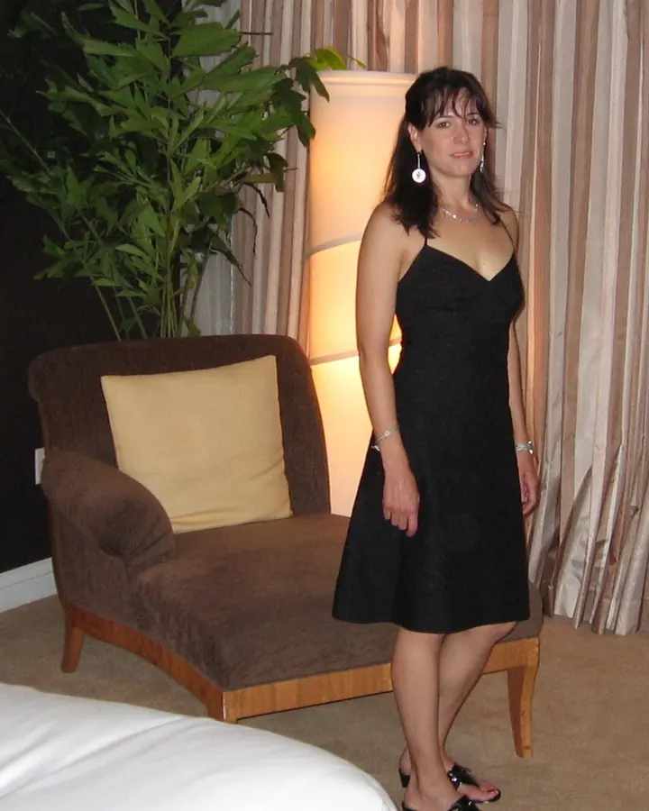 Femme blanche en robe noire, debout près d'un fauteuil, dans une chambre