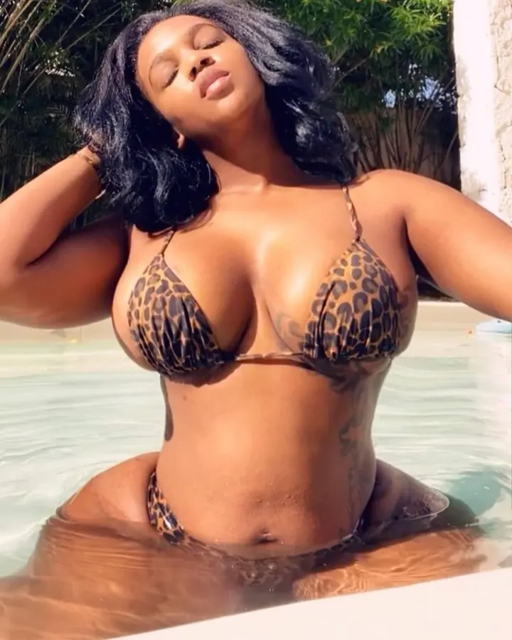 Femme africaine aux cheveux bruns-noirs, peau mate, portant un bikini léopard, assise dans une piscine, yeux fermés.