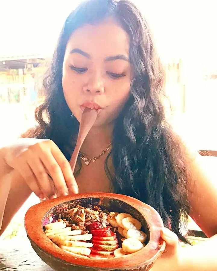 Femme latine en tenue de cuisine, mangeant une salade dans un bol en terre cuite.