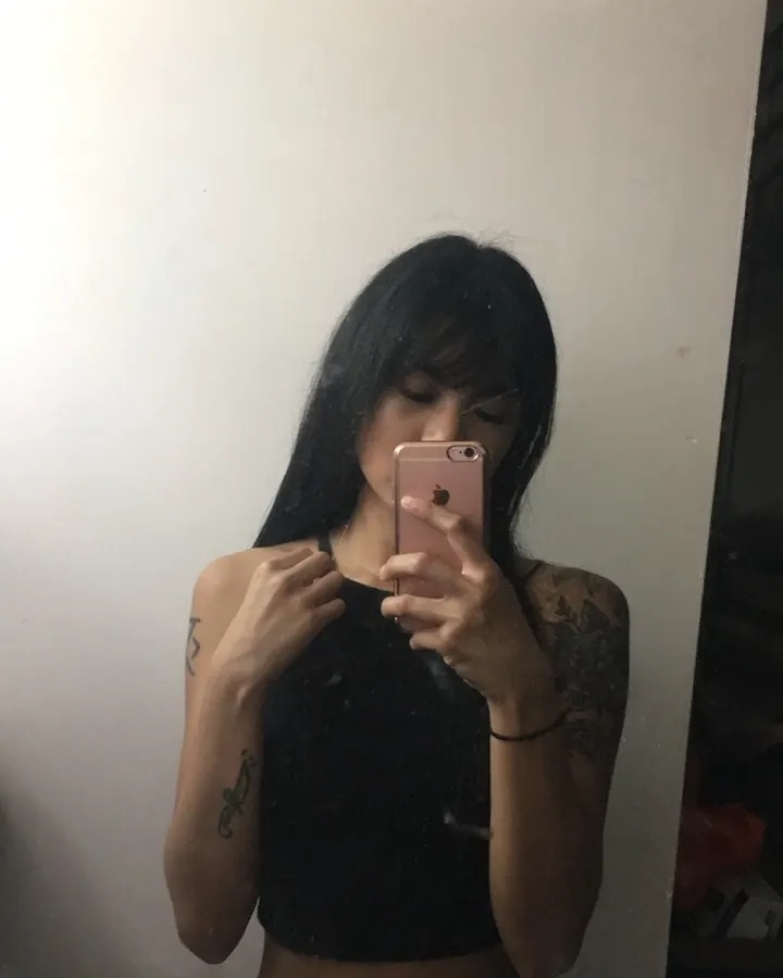 Femme aux cheveux noirs, portant un haut noir et un string rose, prenant un selfie dans un miroir.