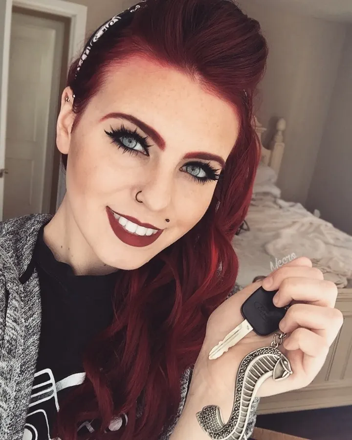 Femme européenne aux cheveux roux, souriante, prenant un selfie devant un miroir avec un haut blanc.