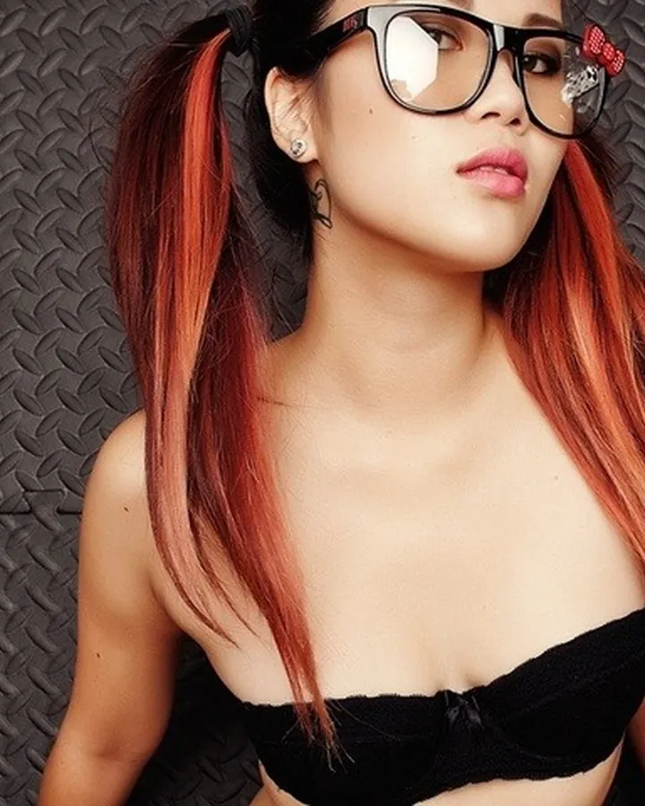 Femme aux cheveux roux, portant un haut vert et une jupe noire, se tenant près d'une porte.